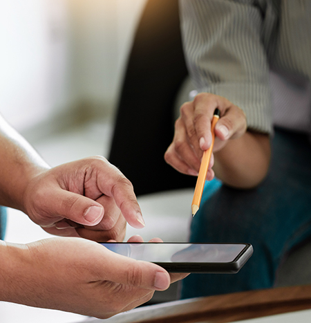 Image of two hands holding a mobile device and another hand pointing at it with a pencil.