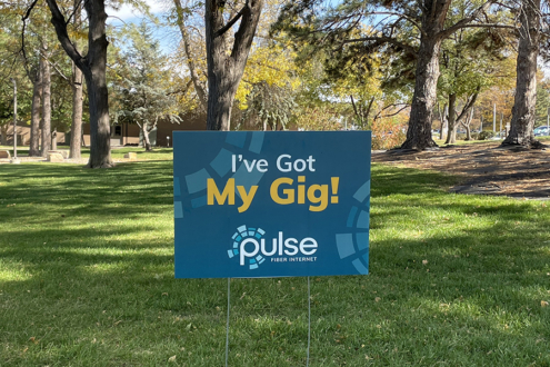Photograph of a yard sign that says I've Got My Gig, placed in a grassy, shaded area.