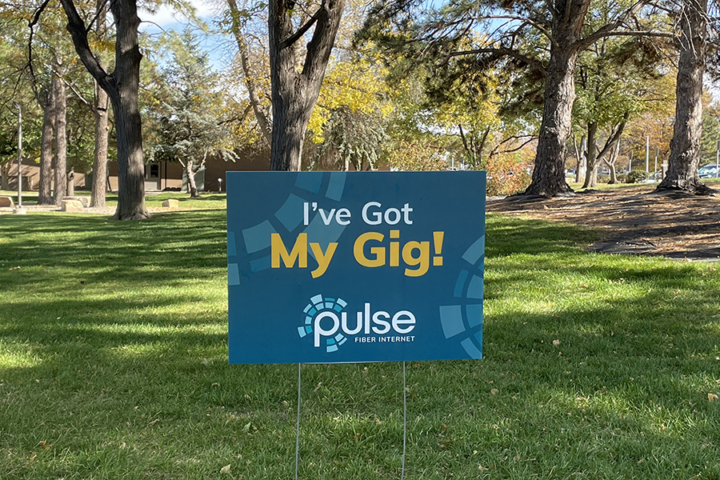 Photograph of a yard sign that says I've Got My Gig, placed in a grassy, shaded area.