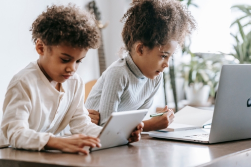 Two kids use devices to do school work online